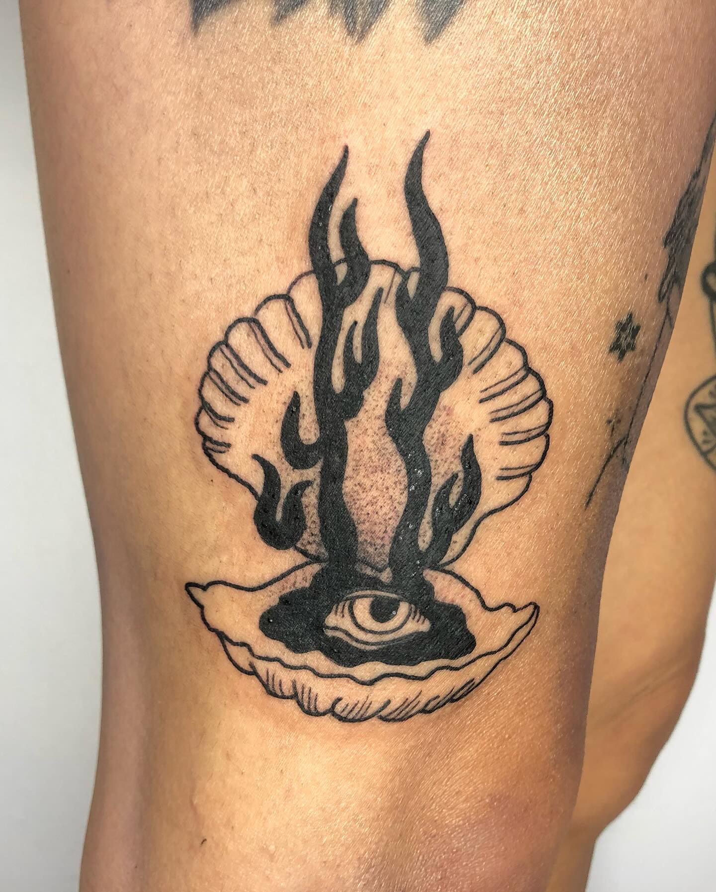 A flame rising from a shell with an eye, tattooed in black